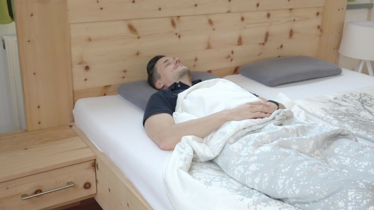 Mann liegt in Rückenlage auf Q-Schlafsystem und schläft mit Rückenschmerzen